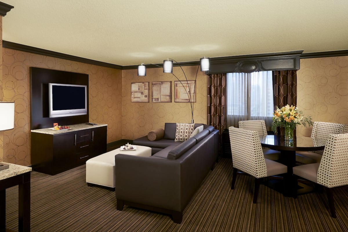Quarto de hotel com sofá, mesa de jantar com cadeiras, televisão, luminária e obras de arte na parede.