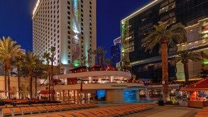 A hotel with a pool area, outdoor seating, and a view of the city skyline at night.