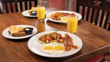 A wooden dining table with plates of breakfast food, including eggs, bacon, toast, and hash browns.