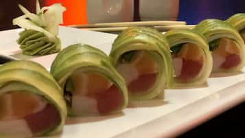 Um prato de sushi com cobertura verde e interior rosa, acompanhado de uma pequena porção de vegetais verdes e uma chávena branca.