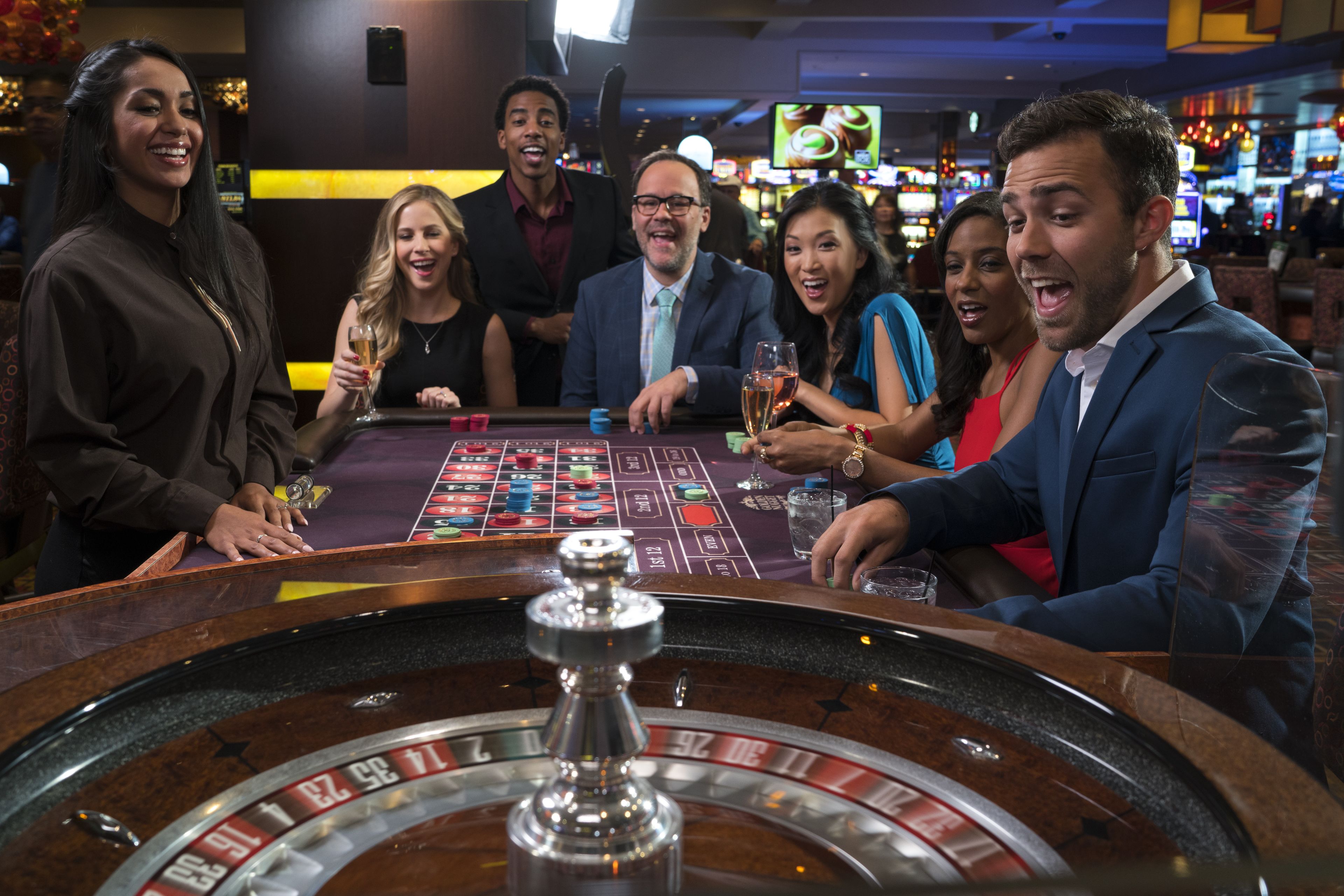A casino floor with a roulette table and slot machines.