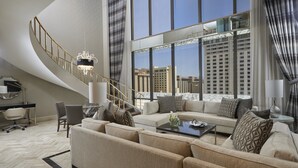 A modern living room with a curved staircase, a sofa set, and a view of the cityscape through large windows.