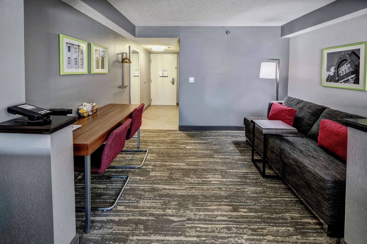 A modern hotel room with a wooden desk, a sofa, and a patterned carpet.