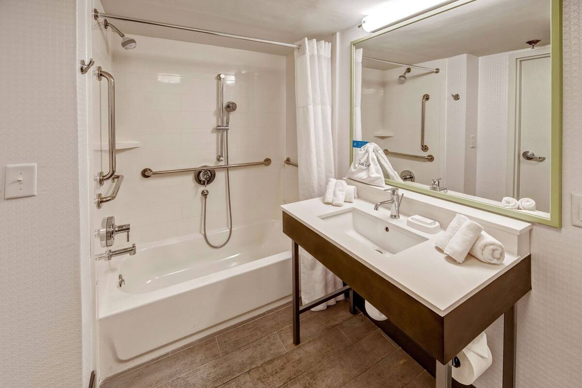 A bathroom with a bathtub, a sink, a mirror, and a towel rack.