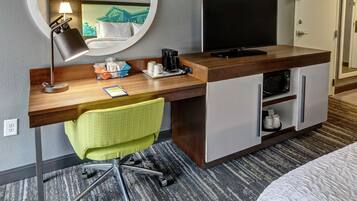 Habitación de hotel con escritorio de madera, una silla de oficina verde, televisor de pantalla plana, cafetera y microondas.