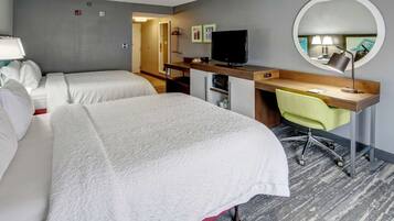 A hotel room with two beds, a desk with a chair, a television, and a round mirror.