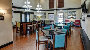 A spacious dining area with wooden flooring, a central bar, and multiple seating options including tables and chairs. - Hampton Inn Batesville (Batesville)