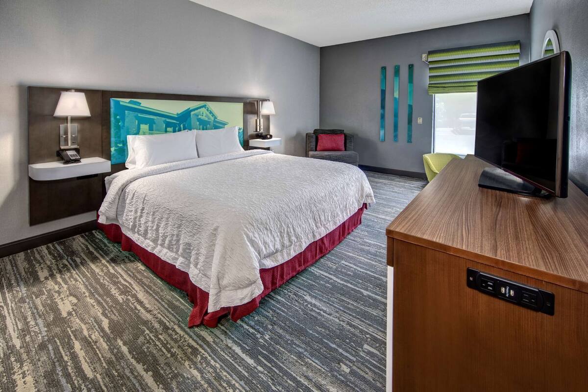 A hotel room with a large bed, bedside lamps, a flat-screen TV, a desk, and a window with blinds.
