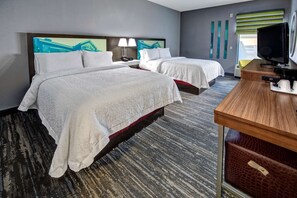 A hotel room with two beds, a desk, a television, and a window with blinds.