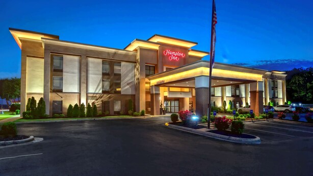 A Hampton Inn hotel with a modern design, featuring a prominent neon sign, a flagpole, and a well-lit entrance. - Hampton Inn Batesville (Batesville)