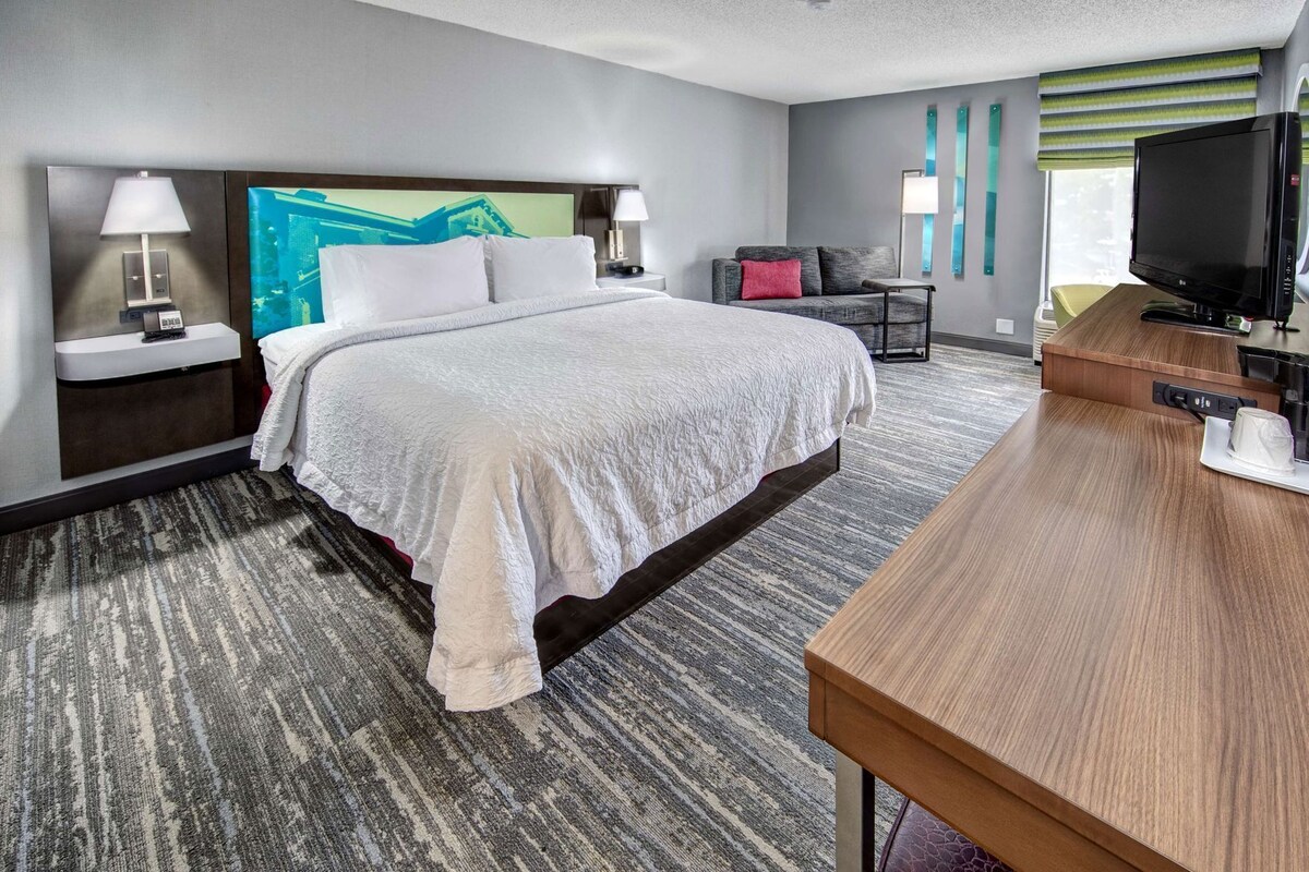 A hotel room with a bed, a desk, a TV, and a nightstand with lamps.