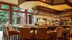 A bar area with multiple stools and a bar counter, large windows, and a view of the outdoors.