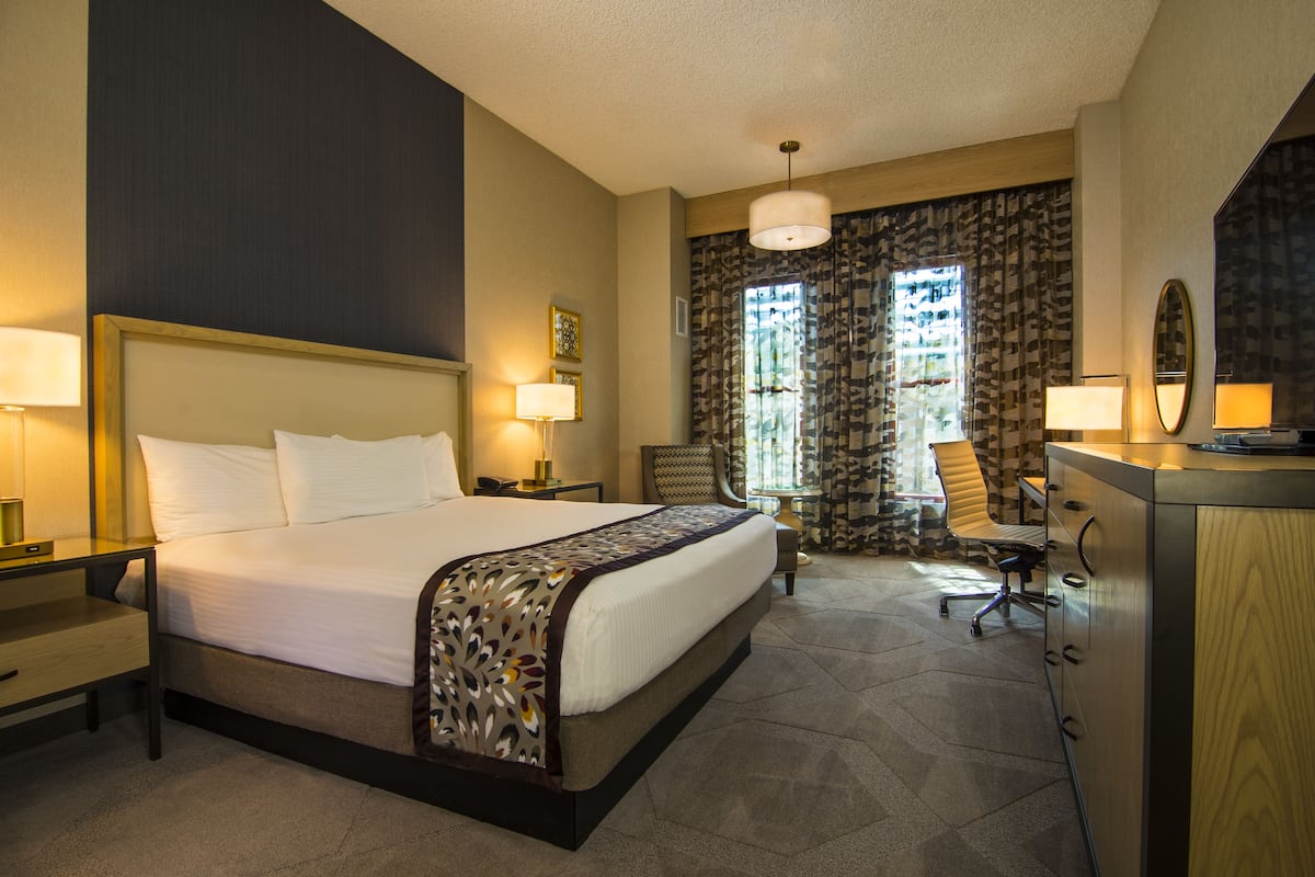 A hotel room with a large bed, a desk, a chair, and a dresser.