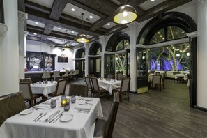 Un restaurant avec des tables recouvertes de nappes blanches, des chaises en bois et un coin bar.