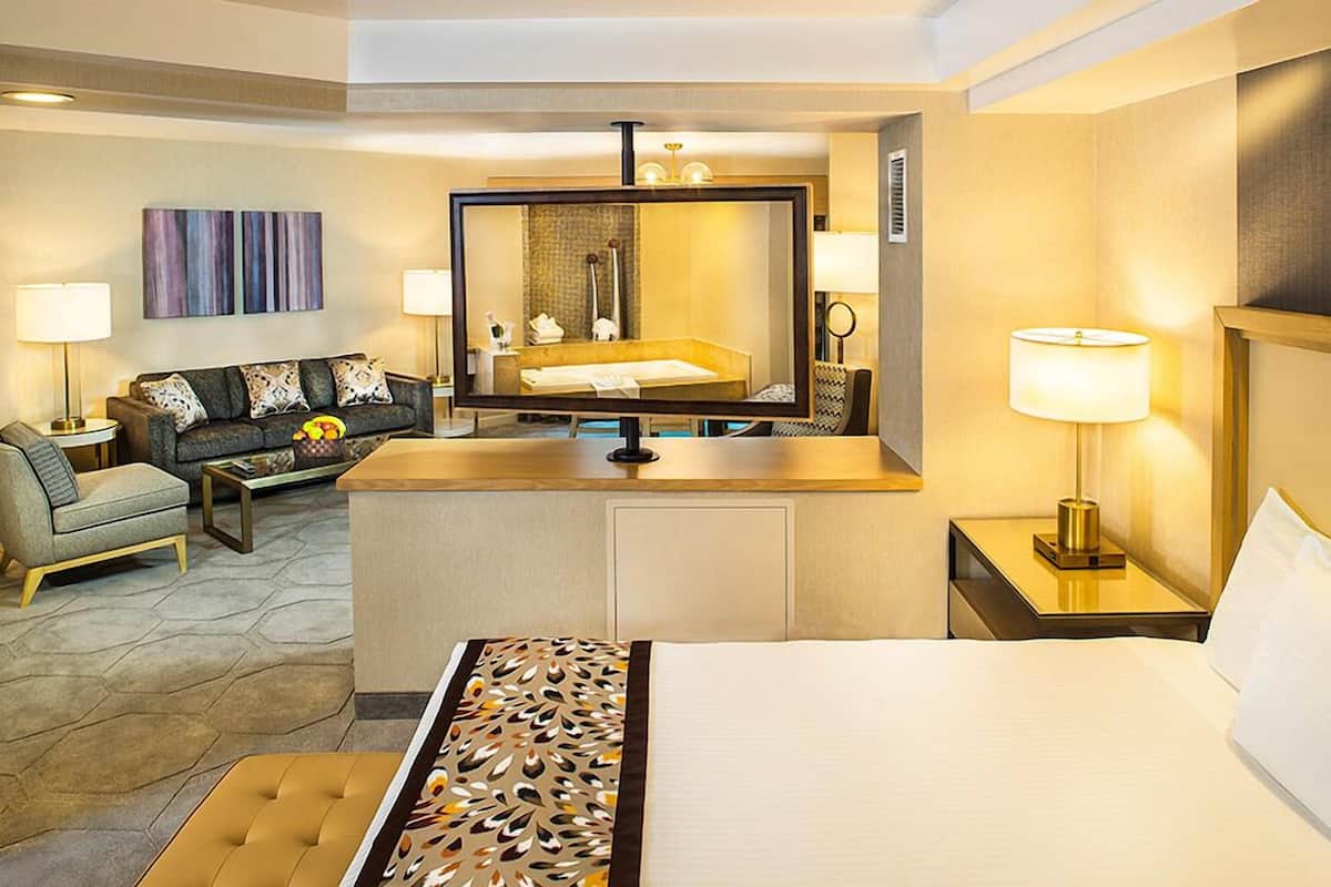 A hotel room with a bed, a sofa, a small table, a mirror, and a lamp.