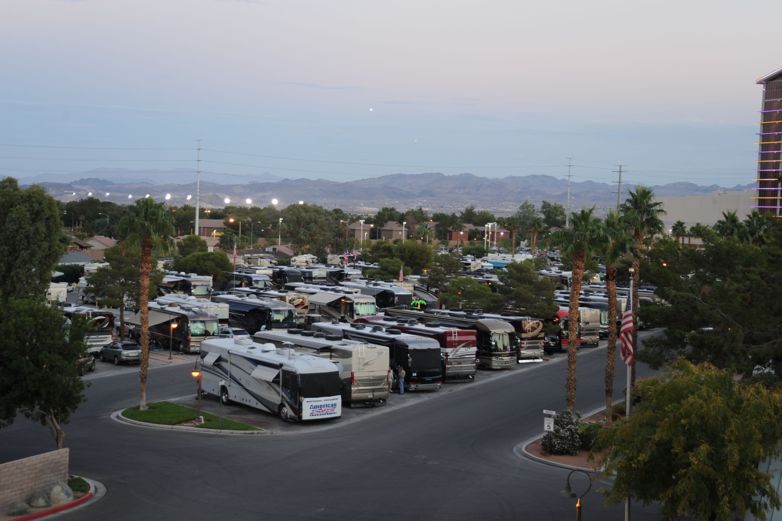 A parking lot with RVs and cars, surrounded by palm trees and buildings.