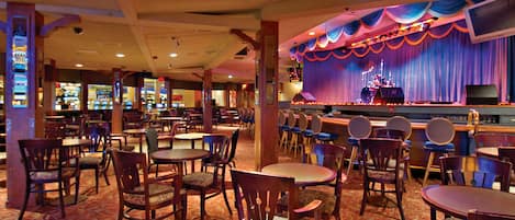 A restaurant with a stage and bar area, featuring wooden tables and chairs, and a patterned carpet.