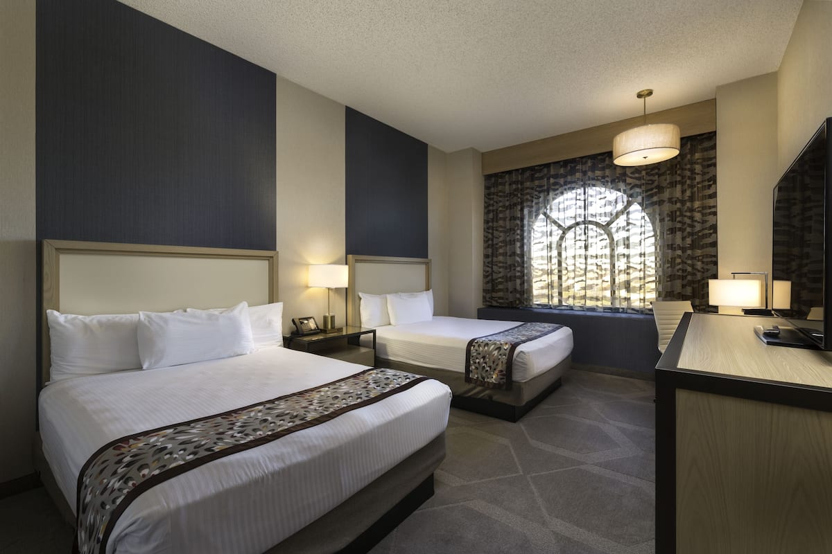 A hotel room with two beds, a desk, and a large window with a view.