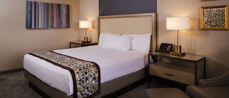 A hotel room with a large bed, two bedside tables with lamps, a desk, and a chair.