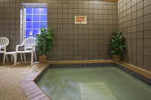 A spa area with a tiled wall, a sign indicating 'OCCUPANT CAPACITY', two white chairs, and two potted plants.