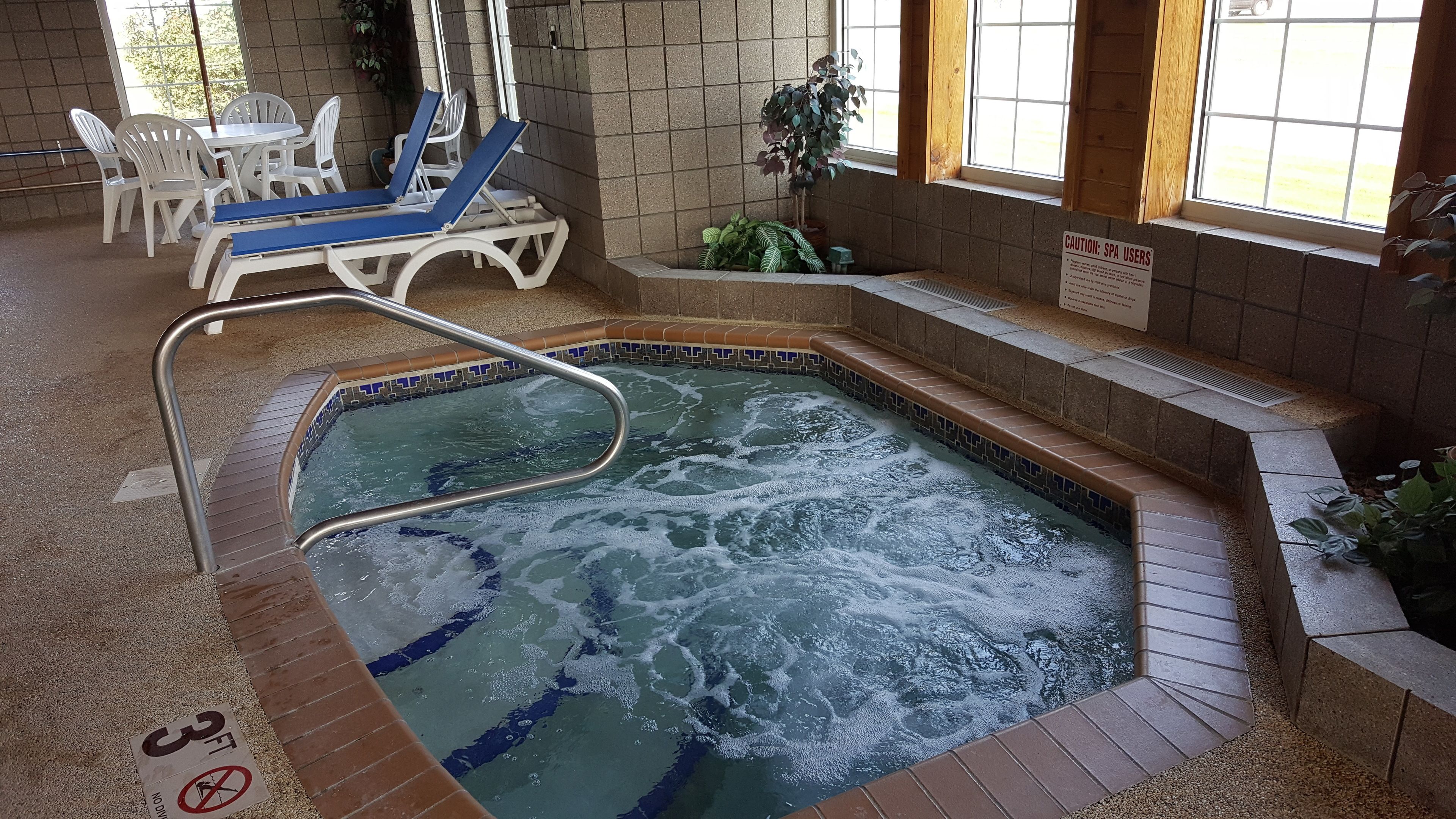 An indoor swimming pool with a hot tub, surrounded by lounge chairs and potted plants.