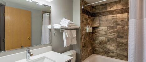 A modern bathroom with a large sink, mirror, and a shower with a stone wall.