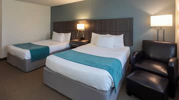 A hotel room with two beds, a desk, a chair, and a lamp.