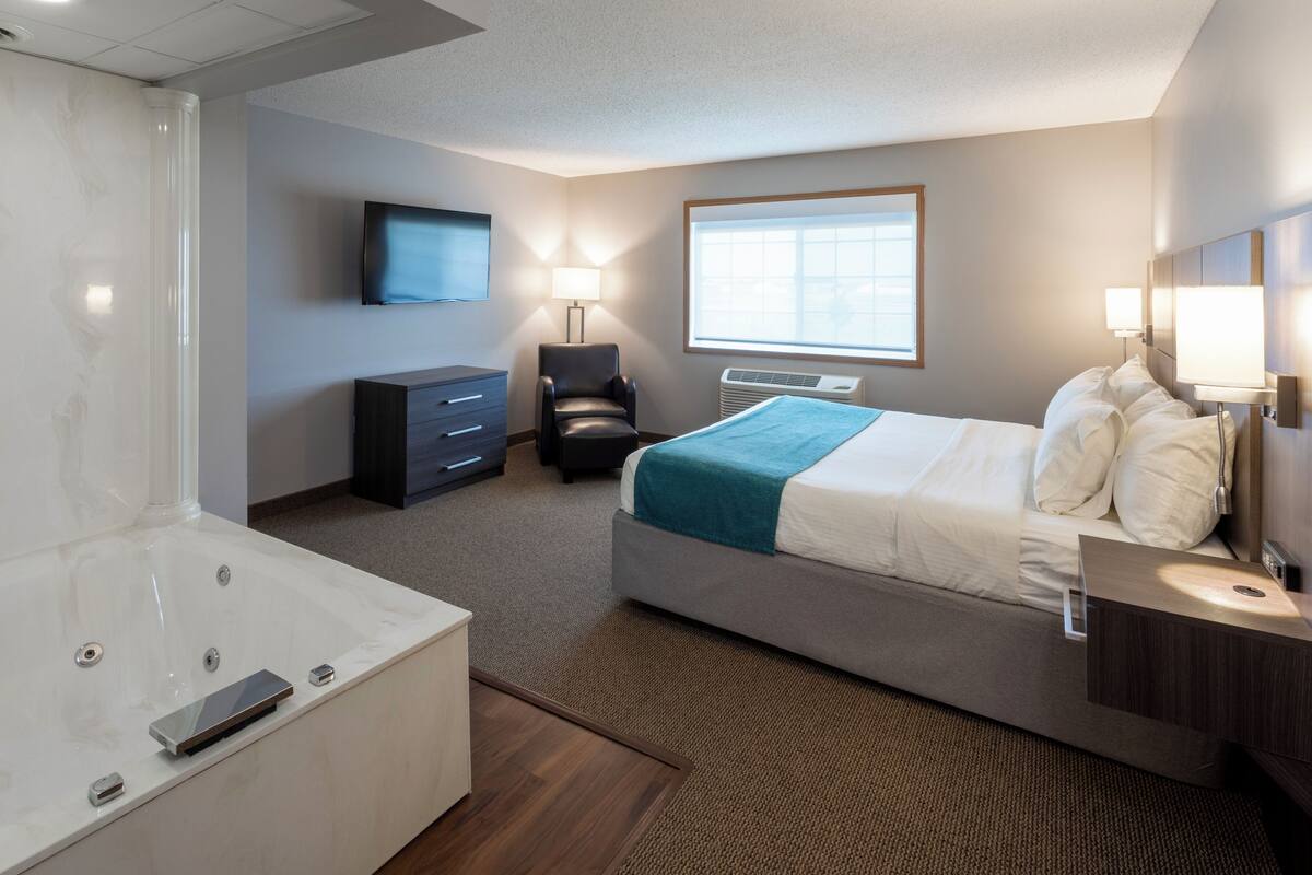 Habitación de hotel con una cama grande, un escritorio, una silla, un televisor y una ventana.