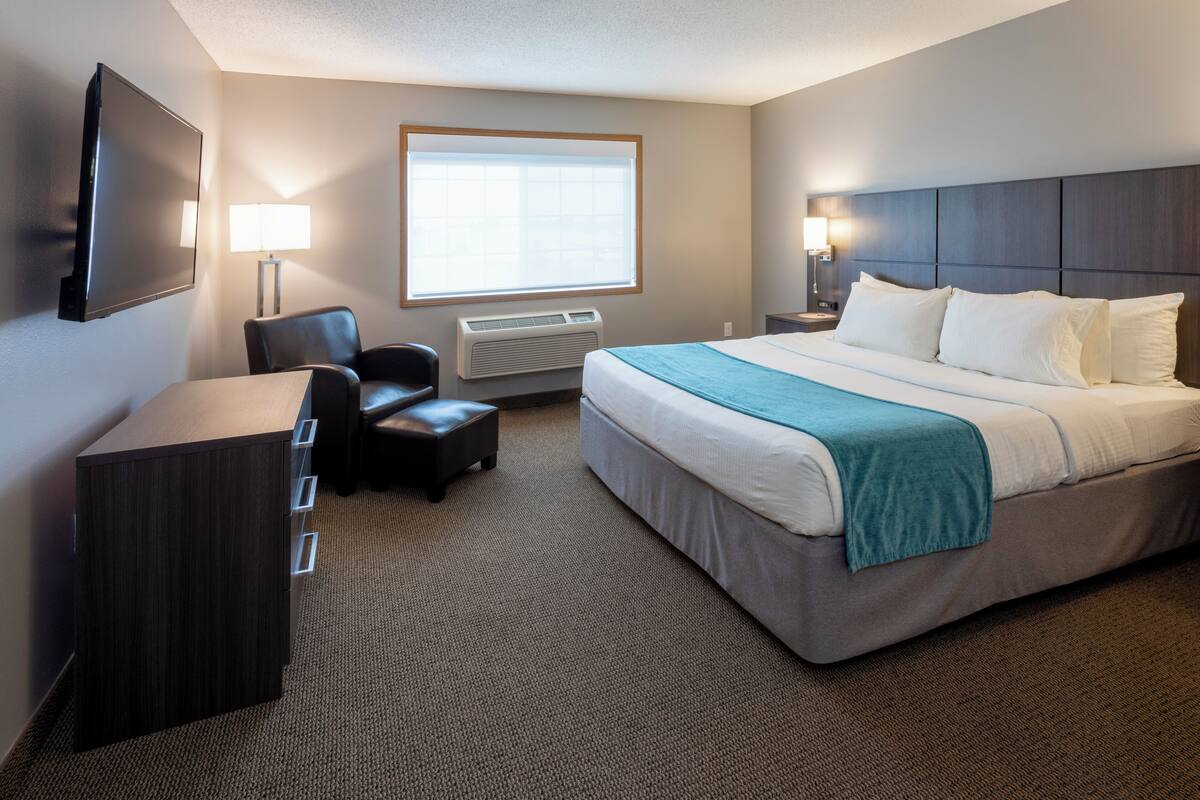 Habitación de hotel con cama, escritorio, silla, televisión y ventana.
