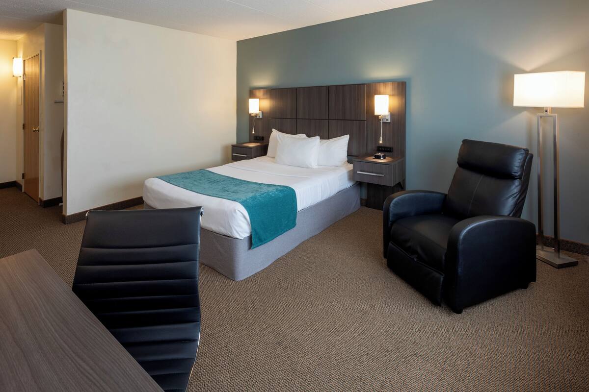 Una habitación de hotel con cama, escritorio, silla y lámpara.
