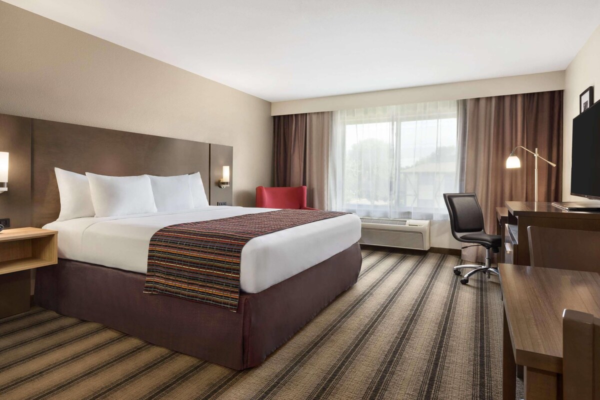A hotel room with a large bed, a desk, a chair, a TV, and a window with curtains.