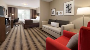 A hotel room with a bed, a desk, a red armchair, a sofa, and a TV. - Country Inn & Suites by Radisson, St. Cloud West, MN (St Cloud)