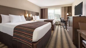 A hotel room with two beds, a desk, a television, and a window with curtains.