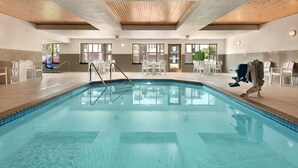 An indoor swimming pool with clear water, surrounded by white chairs and tables, and wooden ceiling beams. - Country Inn & Suites by Radisson, St. Cloud West, MN (St Cloud)