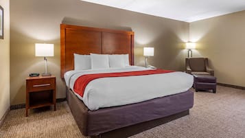A hotel room with a large bed, two bedside lamps, a nightstand, a chair, and a carpeted floor.