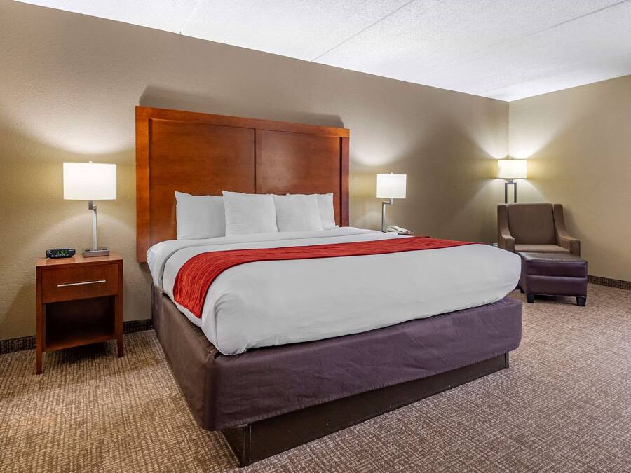 A hotel room with a large bed, two bedside lamps, a nightstand, a chair, and a carpeted floor.