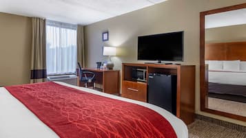 A hotel room with a large bed, a television, a desk with a lamp, and a minibar.