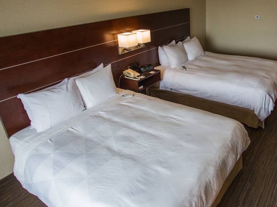 A hotel room with two beds, a nightstand with a phone and a lamp, and a wooden headboard.