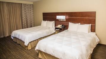 A hotel room with two beds, a nightstand, and a wall-mounted lamp.