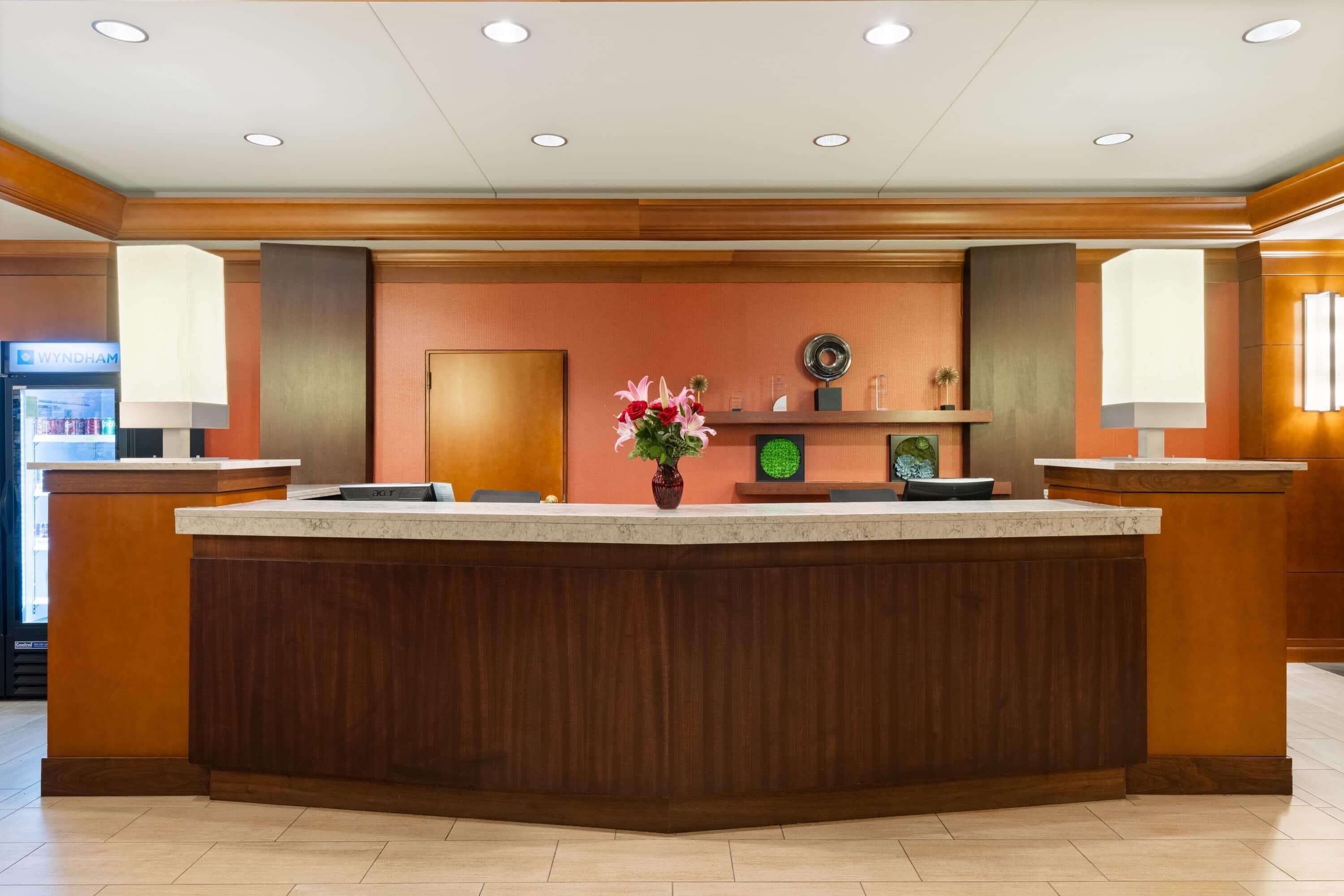 A reception area with a wooden reception desk, a potted plant, a clock, and a refrigerator in the background.