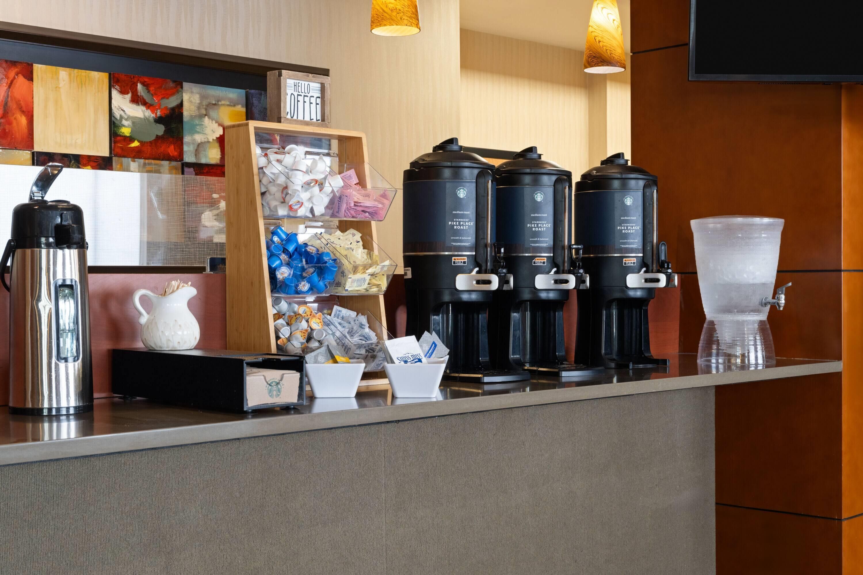 Una estación de café con varias cafeteras, un dispensador de agua y un letrero que dice 'HELLO COFFEE'.