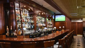 A bar area with a long counter, multiple shelves of bottles, and several chairs.