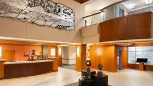 A spacious lobby with a reception desk, a large abstract artwork on the wall, and a modern design with wooden accents.
