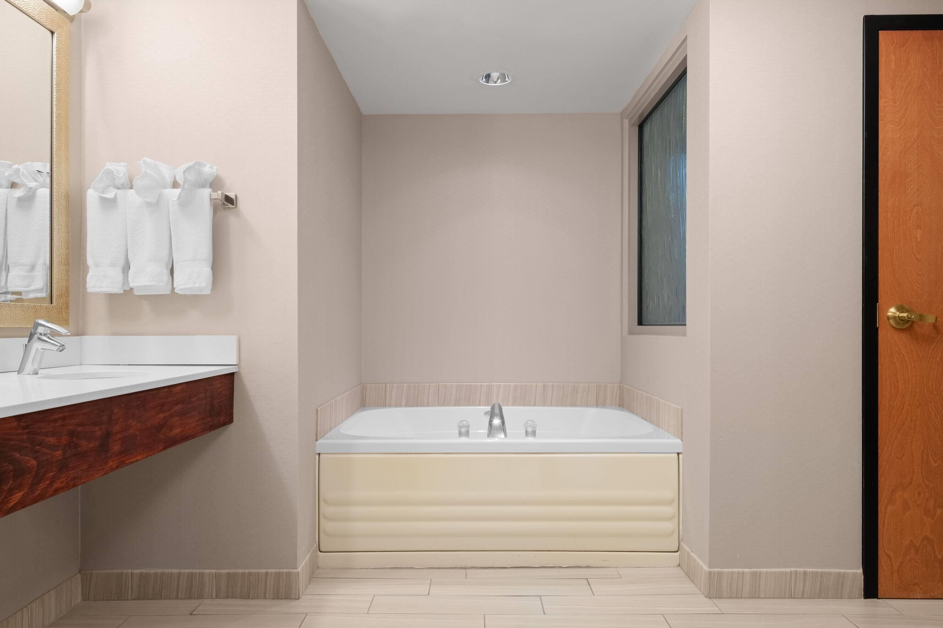 A modern bathroom with a large bathtub, a wooden vanity, and a mirror.