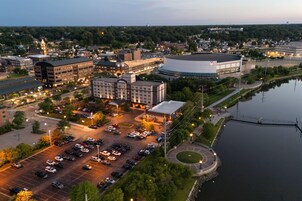 Vista aérea de un paisaje urbano que incluye un estacionamiento amplio, un río y un edificio destacado con techo circular.