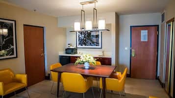 A hotel room with a dining area featuring a wooden table and yellow chairs, a kitchen area with a microwave, and a framed artwork on the wall.