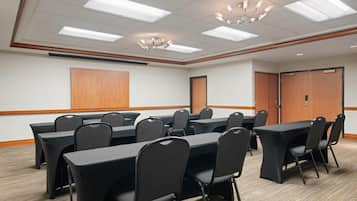 A conference room with multiple tables and chairs, a wooden accent wall, and a ceiling with fluorescent lights.