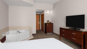 A hotel room with a large bed, a separate bathroom with a bathtub, a wooden dresser, and a flat-screen TV.