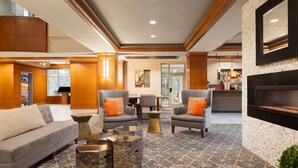 A spacious lobby with a grey sofa, armchairs, and a coffee table. There is a fireplace and a large mirror on the wall.