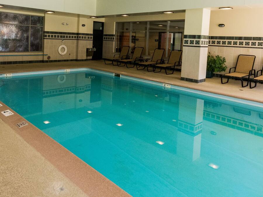 An indoor swimming pool with clear water, surrounded by lounge chairs and a tiled wall with a decorative border.